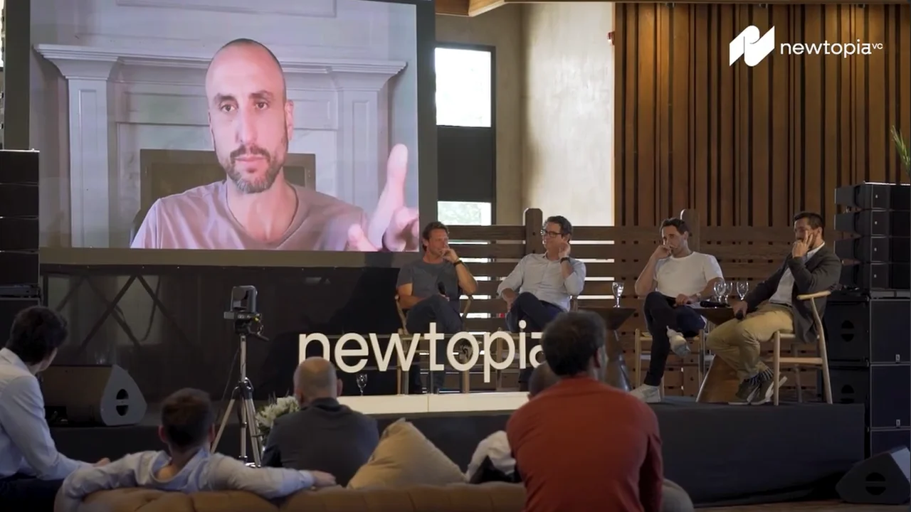 A panel on stage at the Newtopia Summit, with a speaker joining on the screen behind